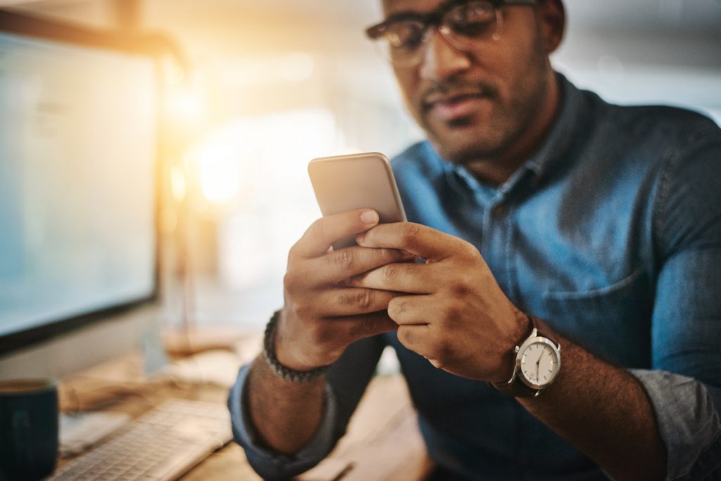Cropped shot of a young businessman using a mobile phone during a late night at work